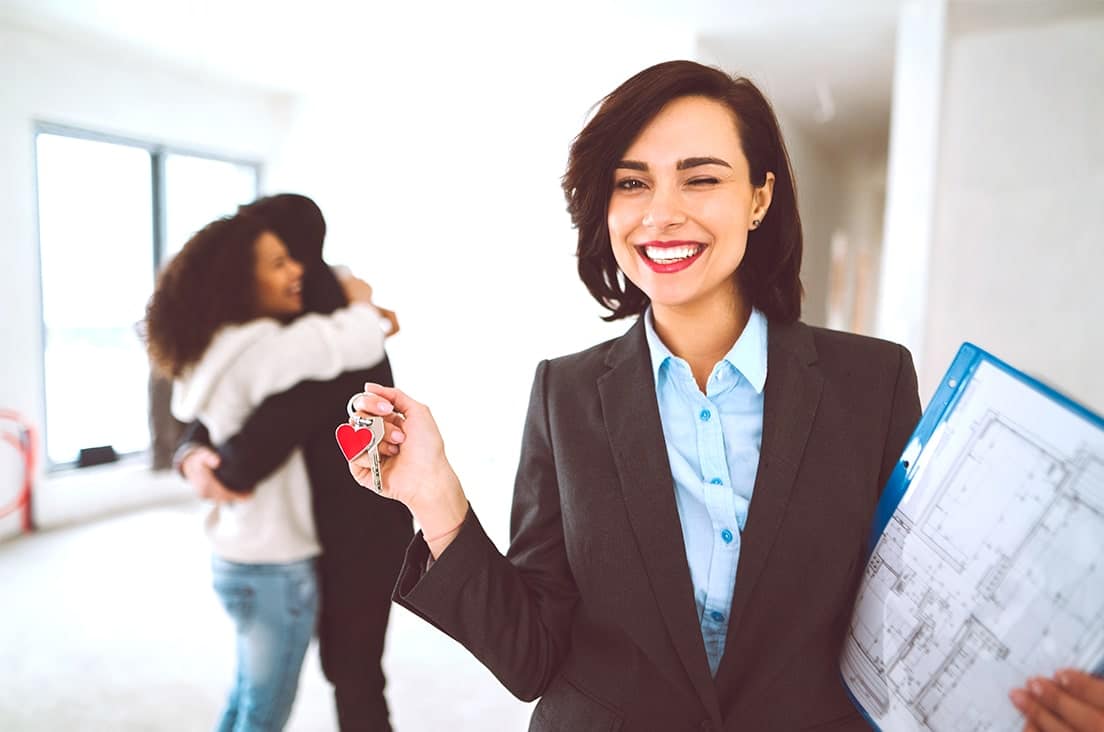 Agent immobilier souriant remettant des clés à des acheteurs dans un logement neuf.
