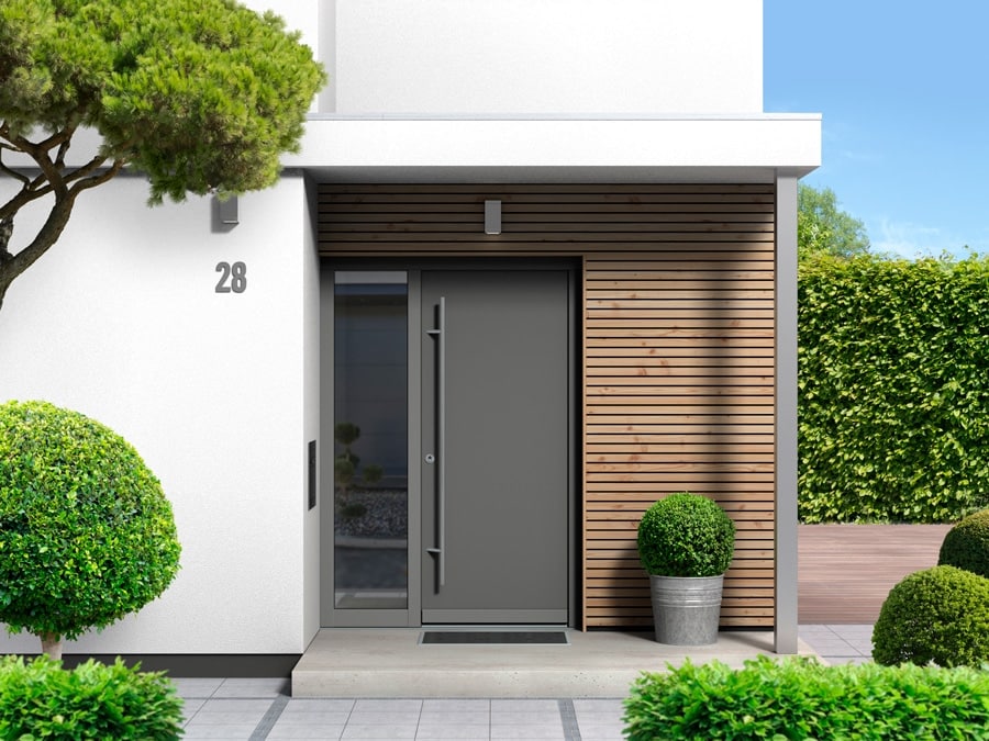 Entrée moderne d'une maison neuve avec porte grise et végétation autour.