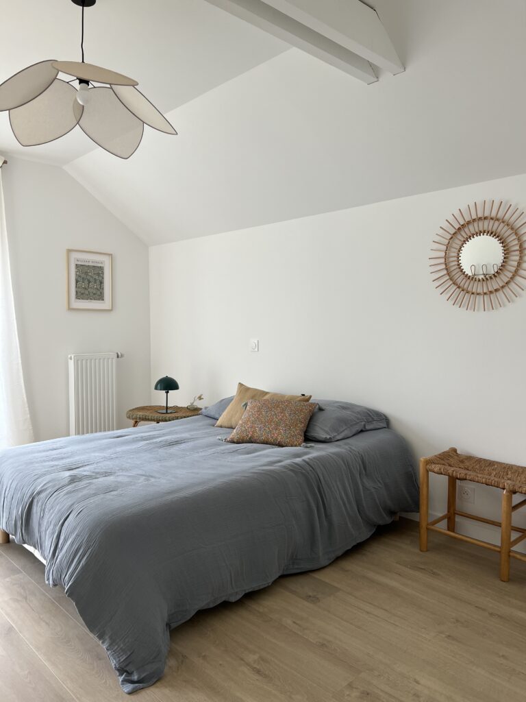 Chambre avec lit, draps gris, et décor en bois naturel.
