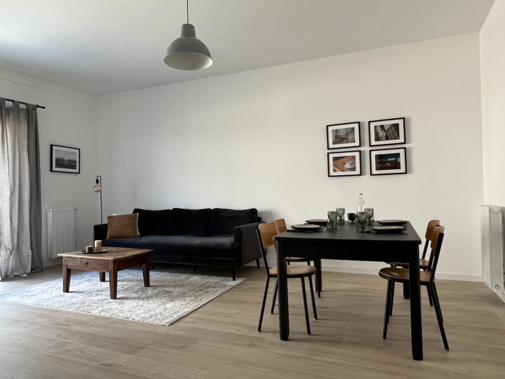 Salon moderne avec canapé noir, table en bois et chaises noires.