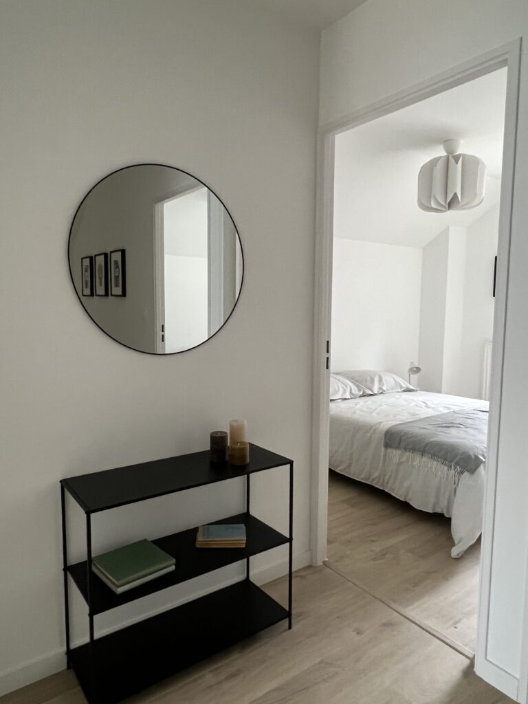 Intérieur d'une maison avec un meuble noir et un miroir rond, offrant une ambiance moderne et lumineuse.