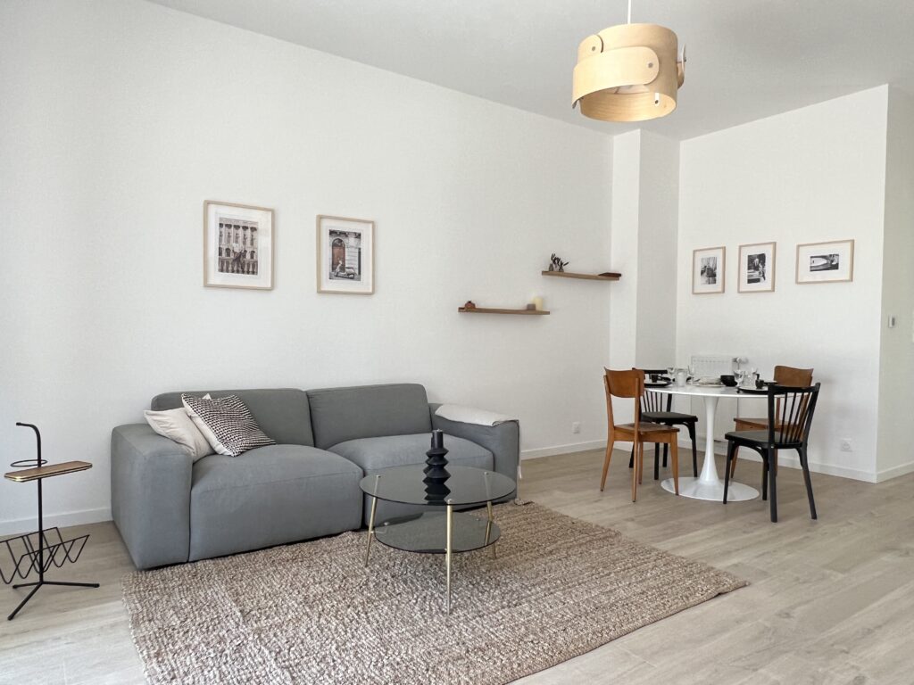 Salon moderne avec un canapé gris, une table ronde et des chaises en bois, décoré de photos au mur.