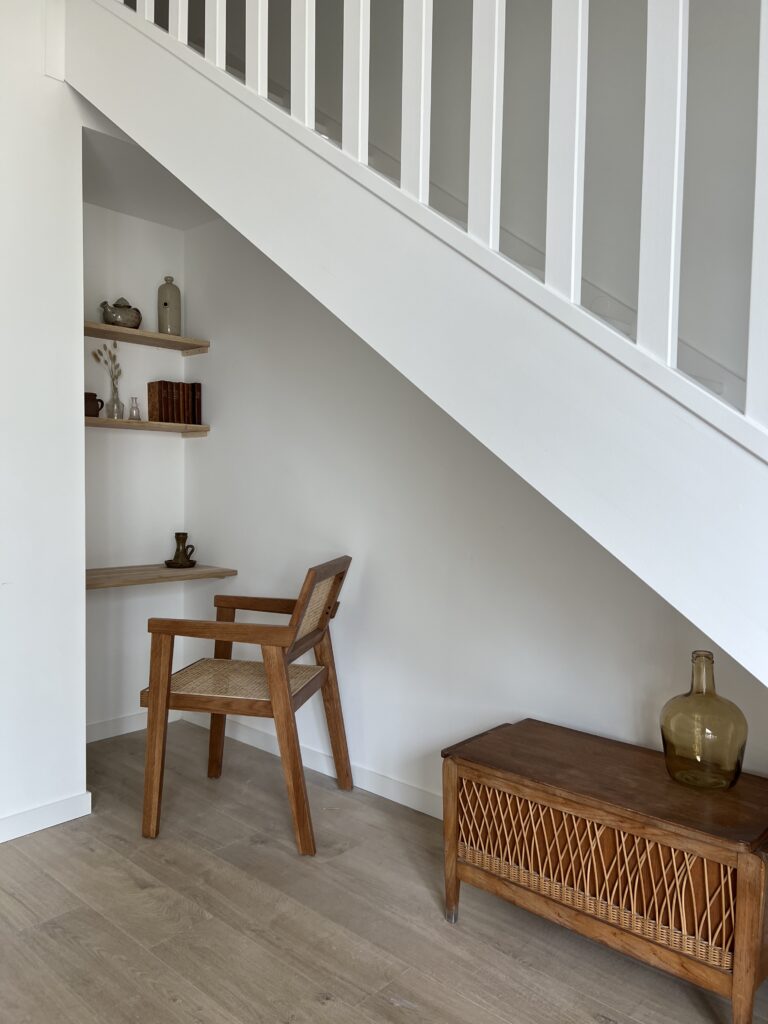Espace sous escalier avec chaise en bois et meuble en osier, ambiance campagne chic.
