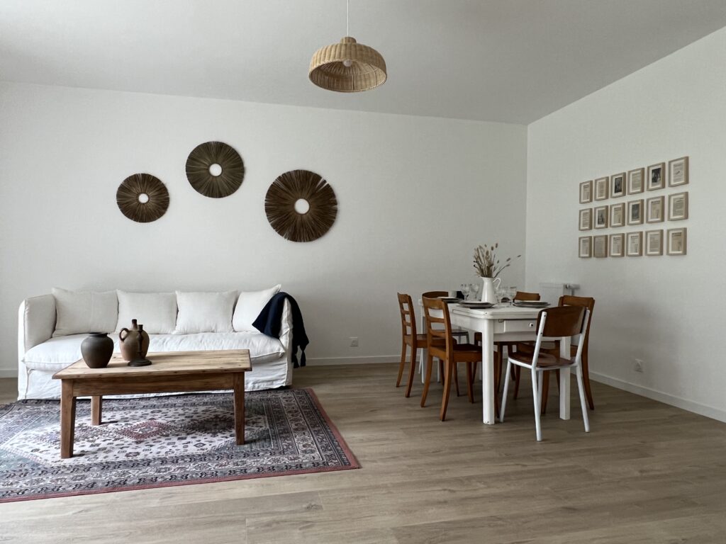 Salon moderne avec canapé blanc, table en bois, et décoration murale en rotin.