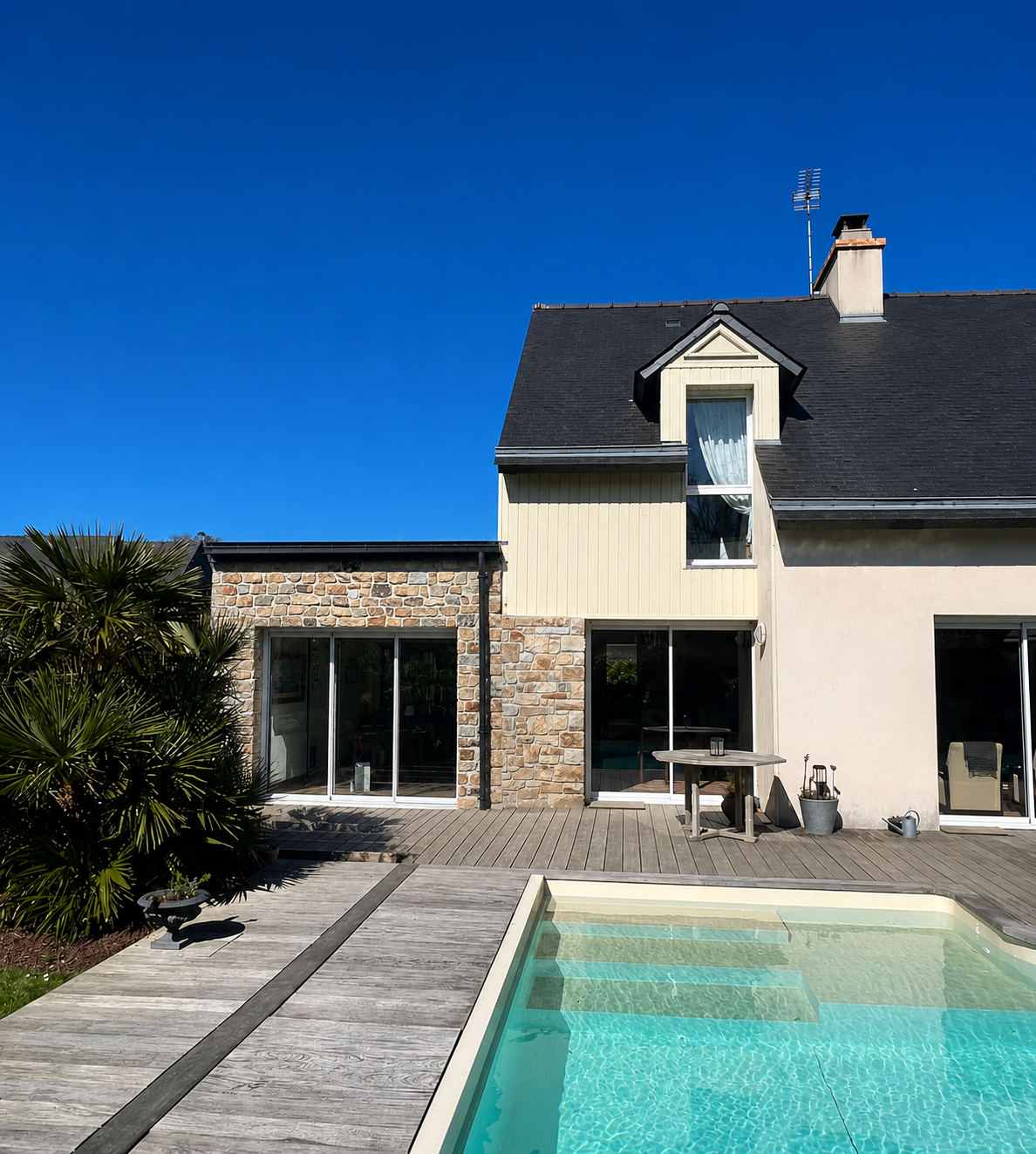 Maison moderne avec piscine et terrasse en bois sous un ciel bleu.